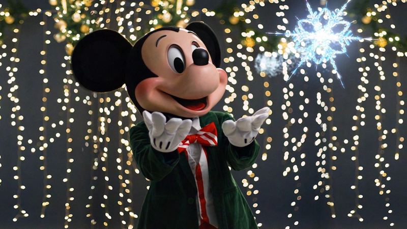 Mickey Mouse in holiday outfit in front of twinkling lights