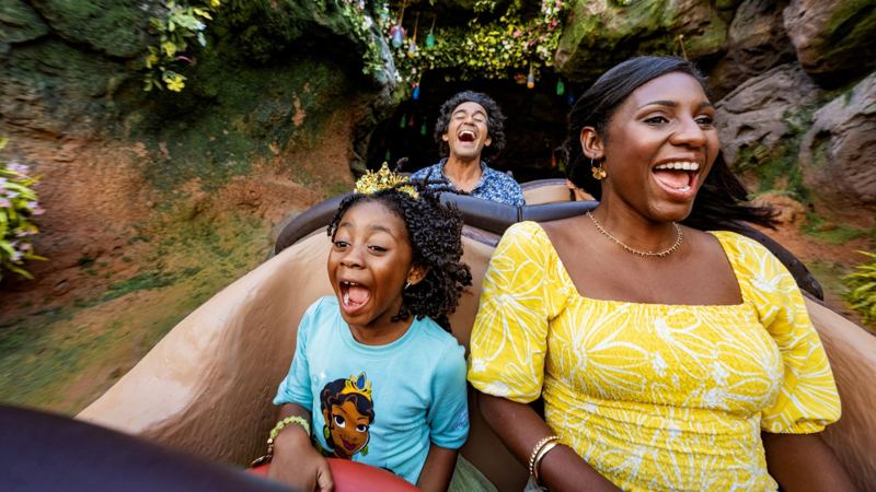 Guests laughing on a log in Tiana's Bayou Adventure