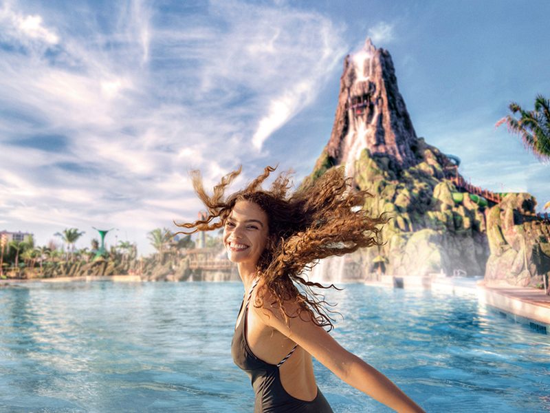 A guest smiling in the Volcano Bay wave pool with the park's volcano behind her